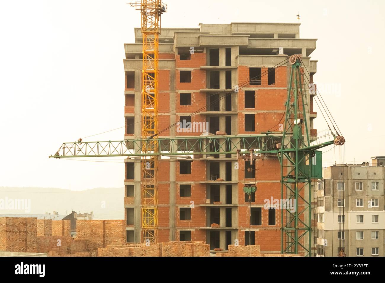 A mid-rise brick building under construction with two cranes working on ...