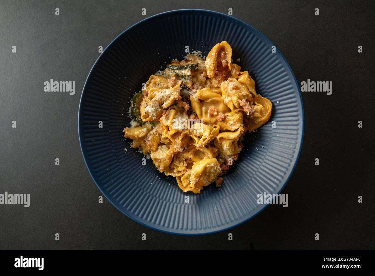 Dish of  Tortellini stuffed pasta with sauce and sprinkled with Parmesan cheese. Top view with rustic black background. Stock Photo