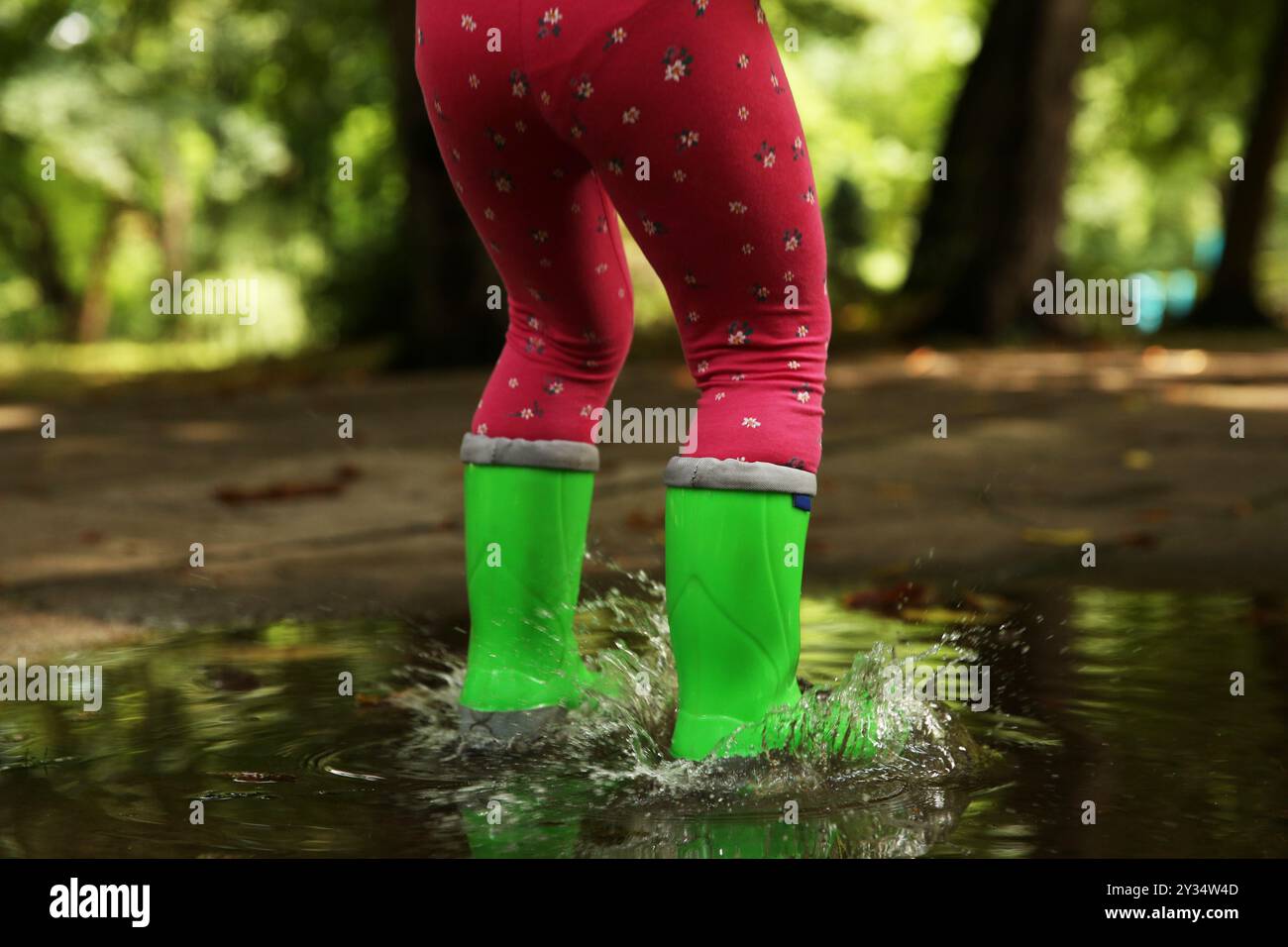 Little girl wearing green rubber boots standing in puddle outdoors ...