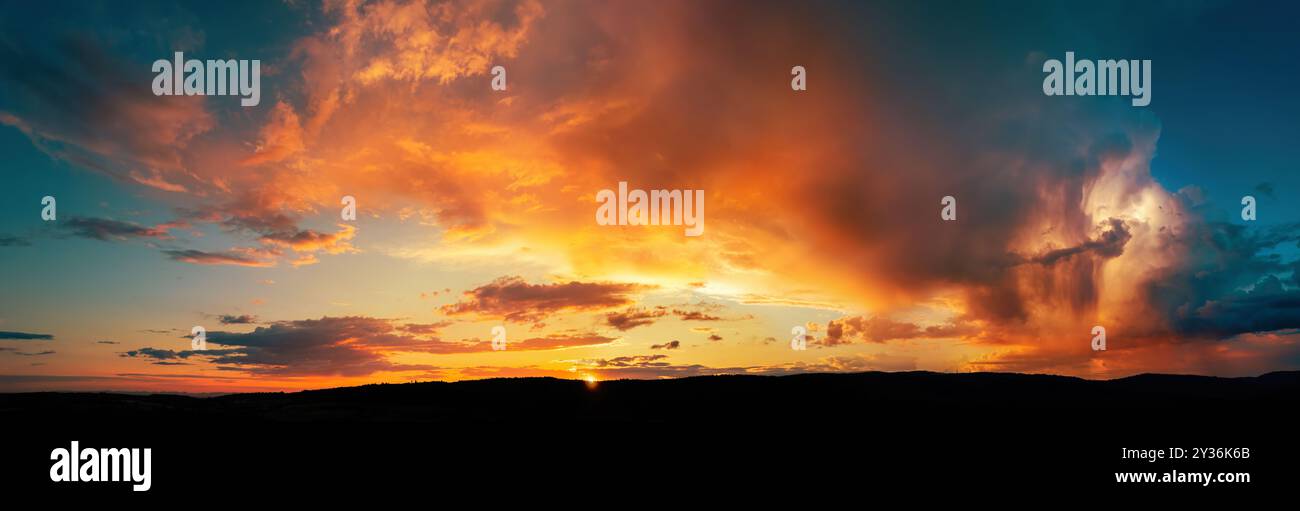 Dramatic storm clouds lit in vivid orange and yellow colors at sunset. A panoramic shot of a weather phenomenon. Stock Photo