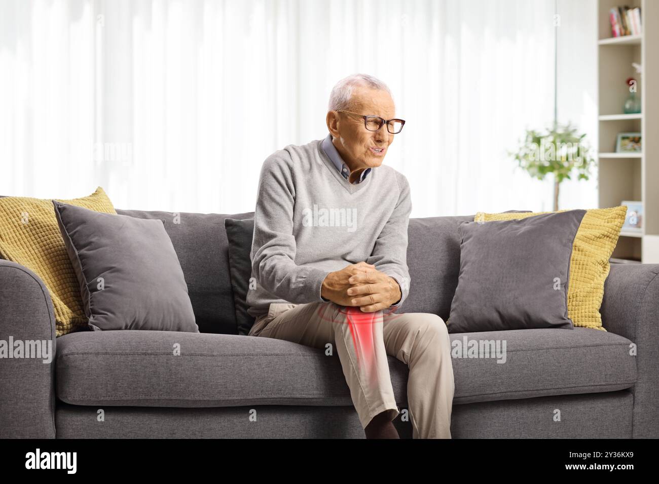 Elderly man with knee pain and red inflamed spot sitting on a sofa Stock Photo