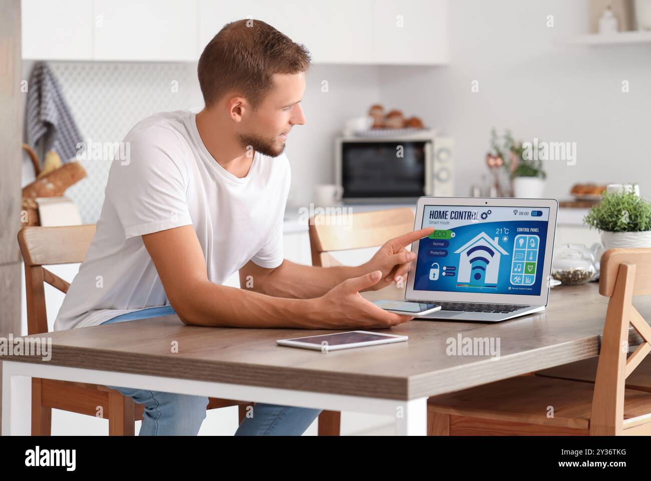 Young man with smart home application on gadgets in kitchen Stock Photo