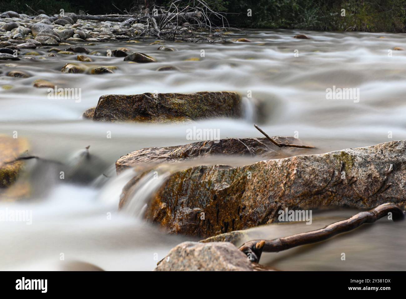 Water flows quickly around rocks in a creek, creating a smooth, silky effect. Stock Photo