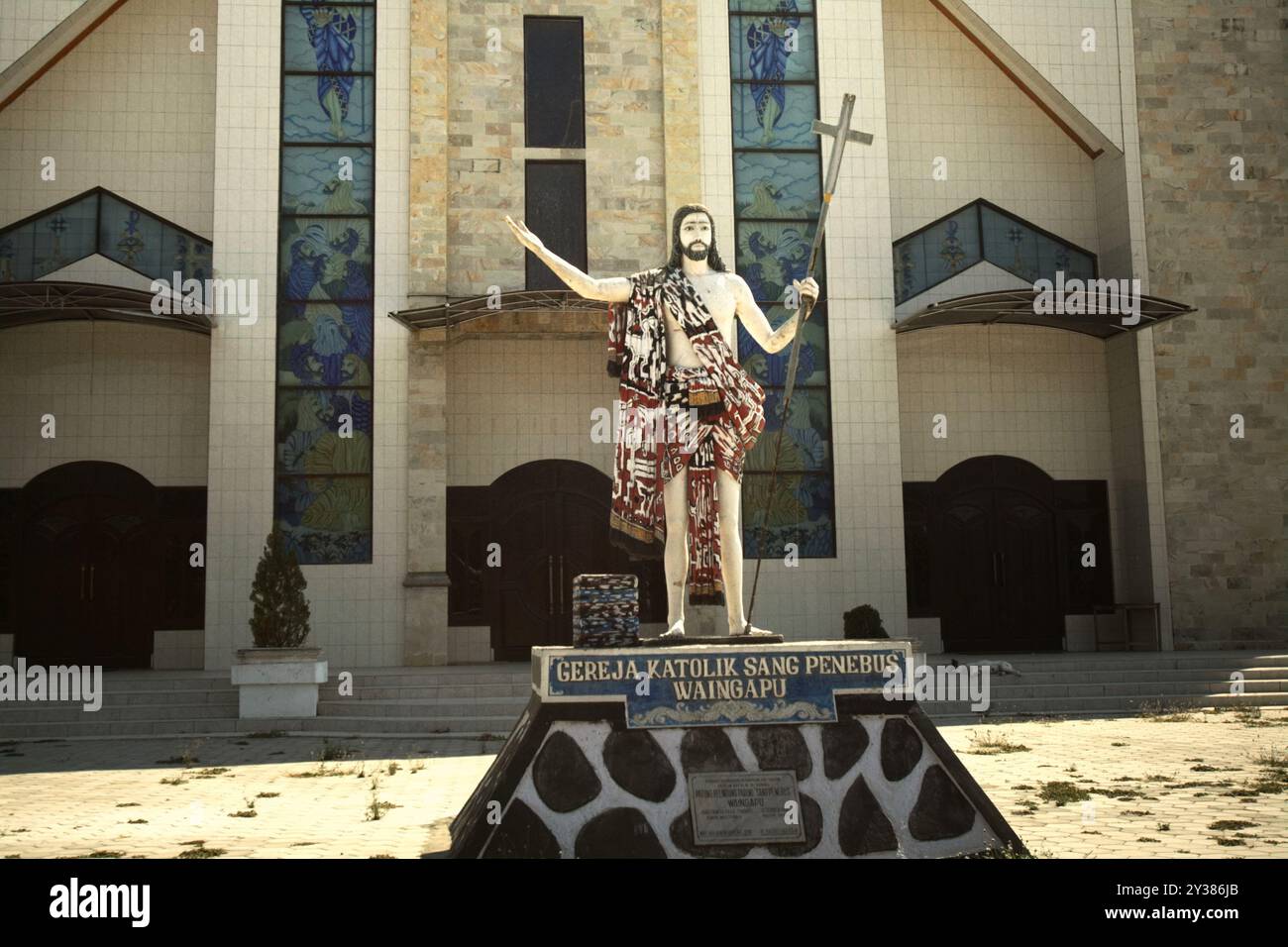 Statue of Jesus holding a cross, wearing Sumbanese textile at the front yard of Gereja Katolik Sang Penebus (Catholic Church of The Redeemer). Stock Photo