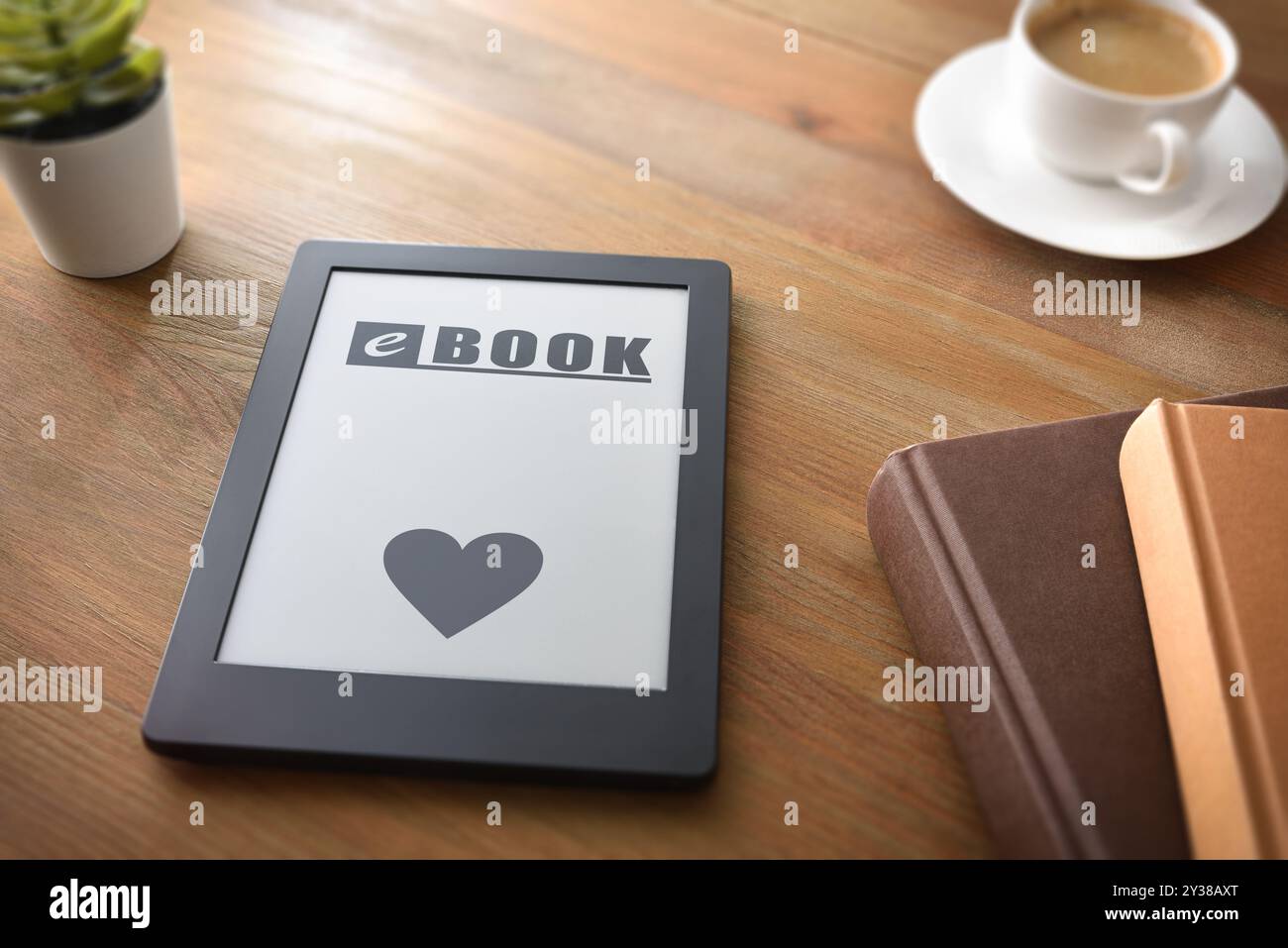 Concept of love for reading with ebook with text on screen and heart on wooden table at home with coffee traditional books and decorations. Elevated v Stock Photo