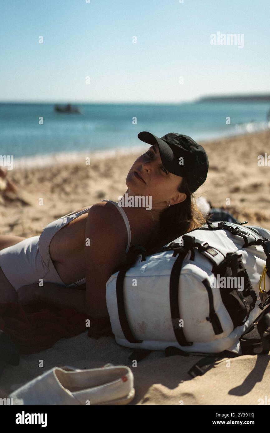 A woman in a baseball cap sunbathes on a sandy beach. Stock Photo