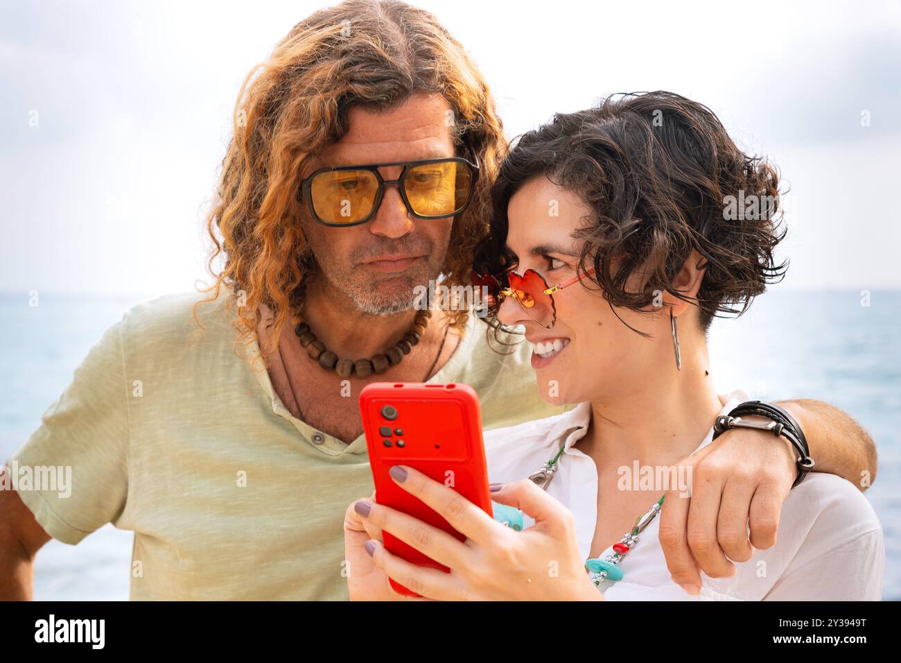 Smiling couple on the beach browsing smartphone apps. Stock Photo