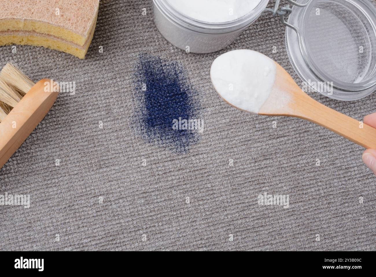 A woman's hand using natural ingredients baking soda to remove ink stains on gray textured upholstery of a sofa or carpet. top view. High quality phot Stock Photo