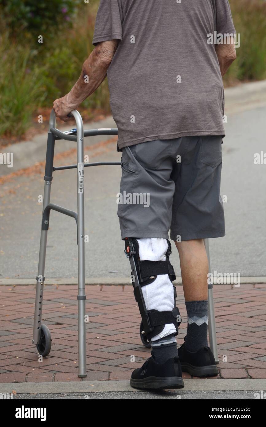 A man wearing a Bregg post-op orthopedic knee brace walks with the aid of a walker in Hendersonville, North Carolina. Stock Photo