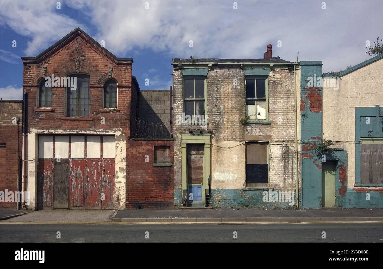 Derelict houses and abandone garage on a residential street with boarded up windows and decaying crumbling walls Stock Photo