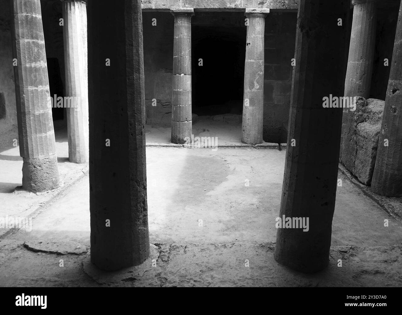 Monochrome image of an underground chamber at the tombs of the kings in paphos cyprus with old eroded sandstone columns surrounding a dark empty doorw Stock Photo