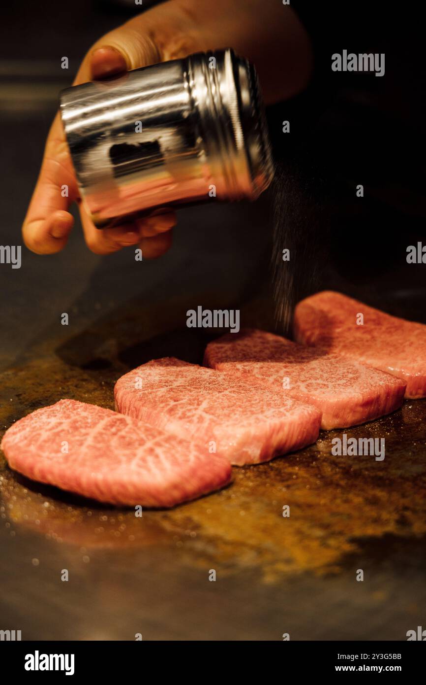 Raw A5 Japanese wagyu steak being seasoned and cooked on grill in an