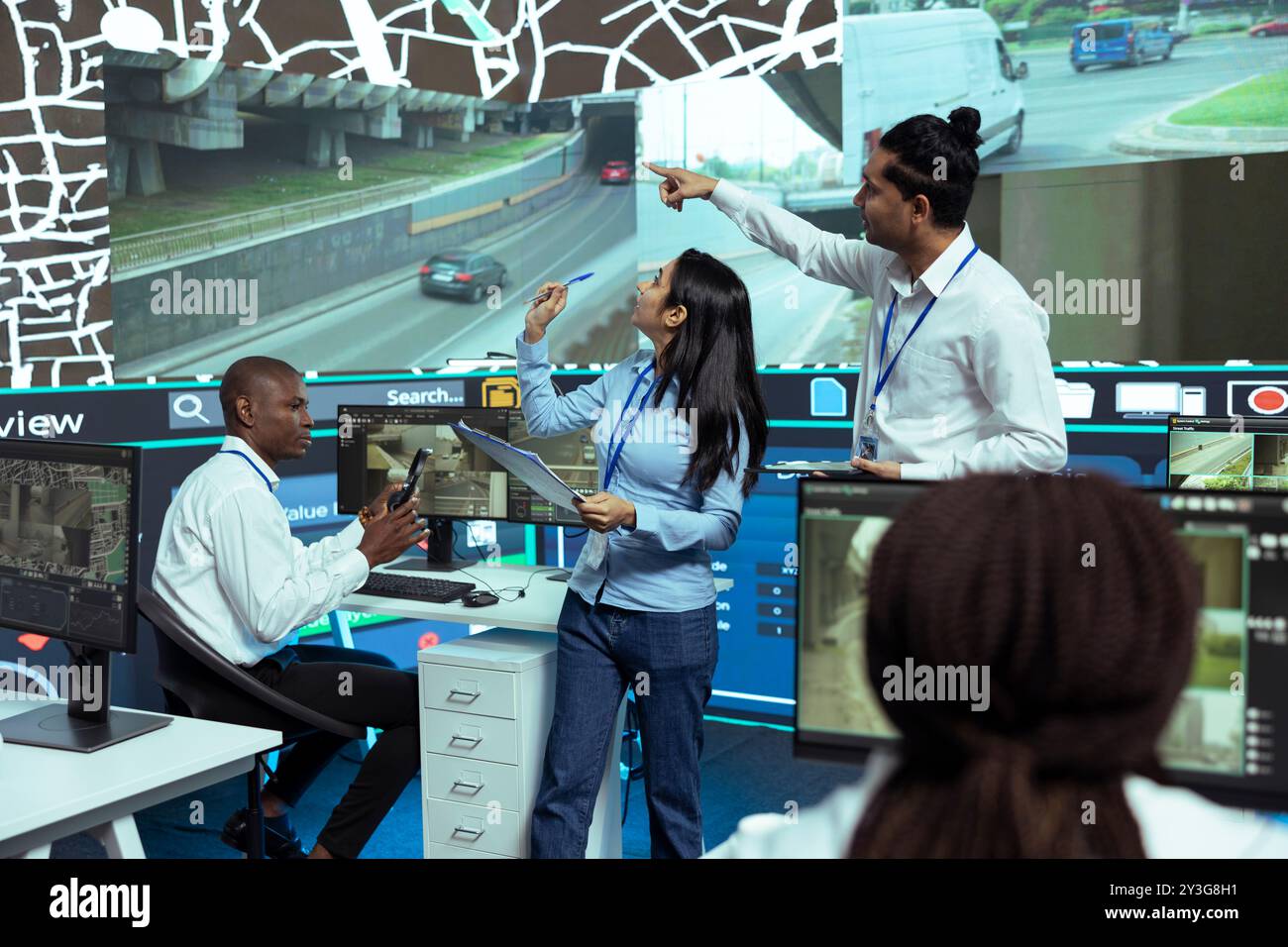 Indian managers instructing their staff how to use CCTV footage and provide gps coordinates to couriers. Monitoring room operators using satellite map for order tracking, cargo surveillance. Stock Photo