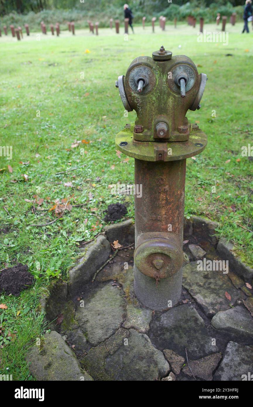 Schwesing, Schleswig-Holstein Hydrant auf dem Gelände der KZ-Gedenkstätte Husum-Schwesing. Im Hintergrund Stelenfeld mit Personen. SS-Männer und manche Kapos nutzten den Hydranten zur Misshandlung der Häftlinge. Im KZ Husum-Schwesing wurden während der NS-Zeit 297 Menschen ermordet. Aufnahme vom 13.09.2024, Schwesing, Nordfriesland *** Schwesing, Schleswig Holstein Hydrant on the grounds of the Husum Schwesing concentration camp memorial site In the background field of stelae with people SS men and some Kapos used the hydrant to abuse the prisoners 297 people were murdered in the Husum Schwesi Stock Photo