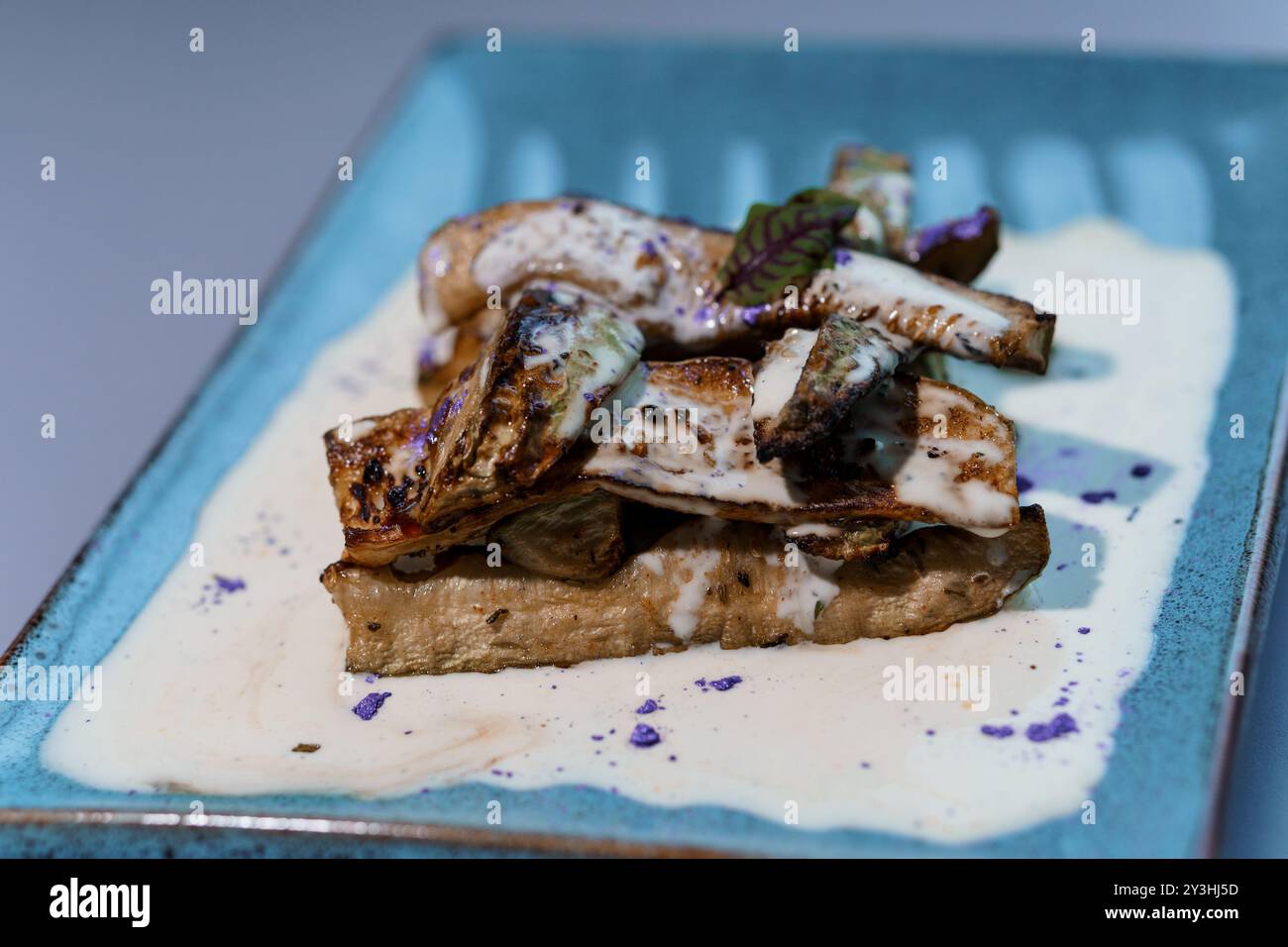 Gourmet Artistry: Savory Grilled Mushrooms on Creamy Sauce with Purple Garnish on Elegant Blue Plate. Stock Photo