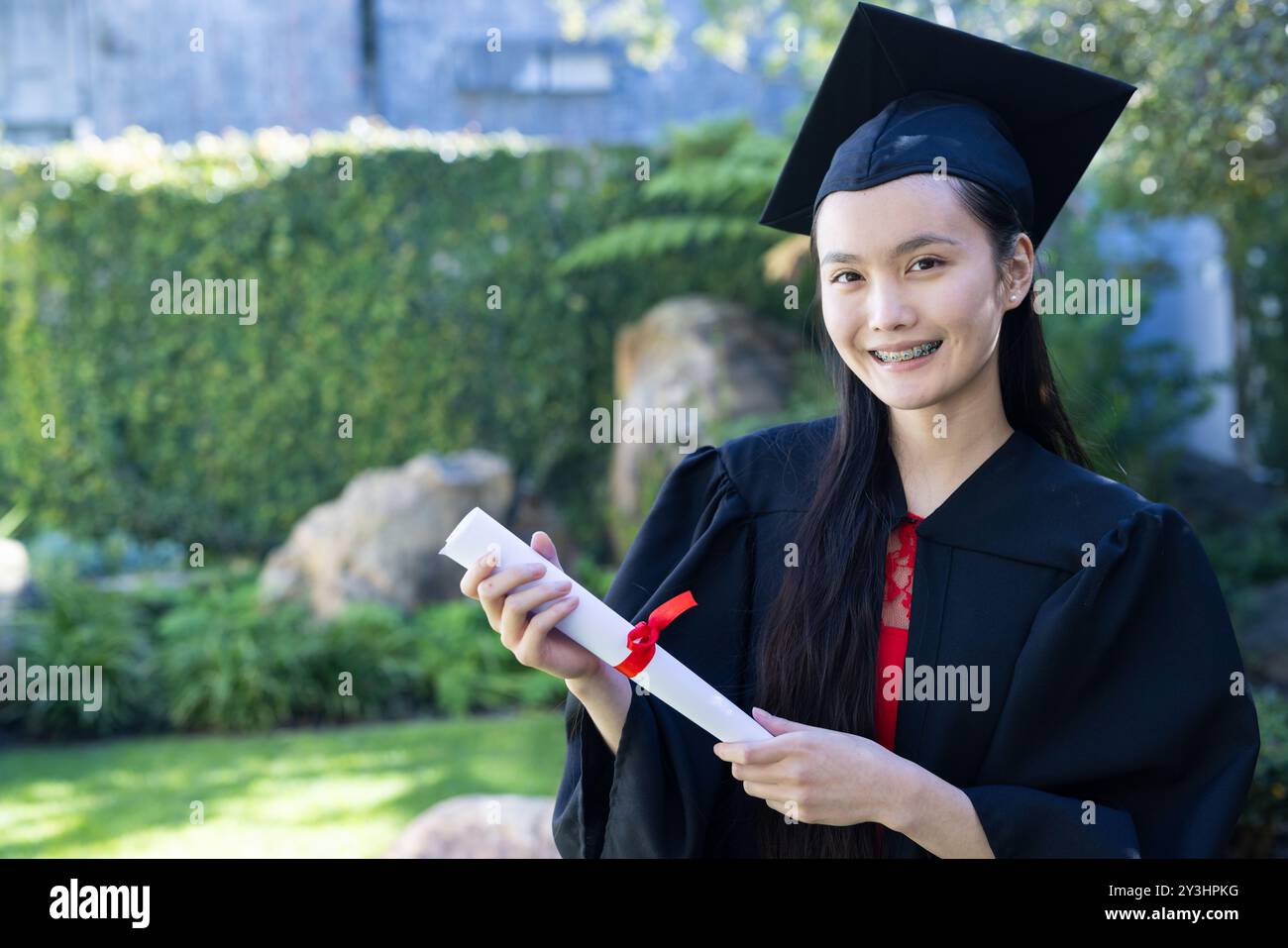 In garden, Graduating asian young woman holding diploma and smiling ...