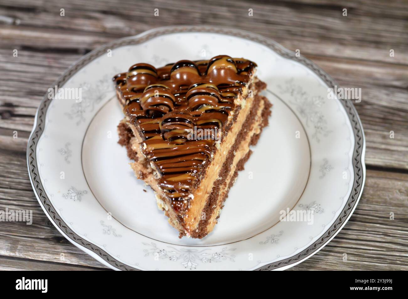 A chocolate triangular spongy cake piece filled and topped with layers ...