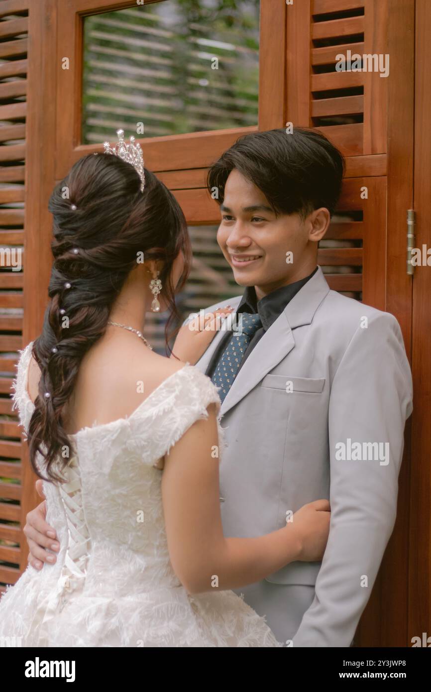 a pair of men and women in elegant poses standing in formal casual poses in  front of a wooden wall looking cross-legged in beautiful dresses in a park  Stock Photo