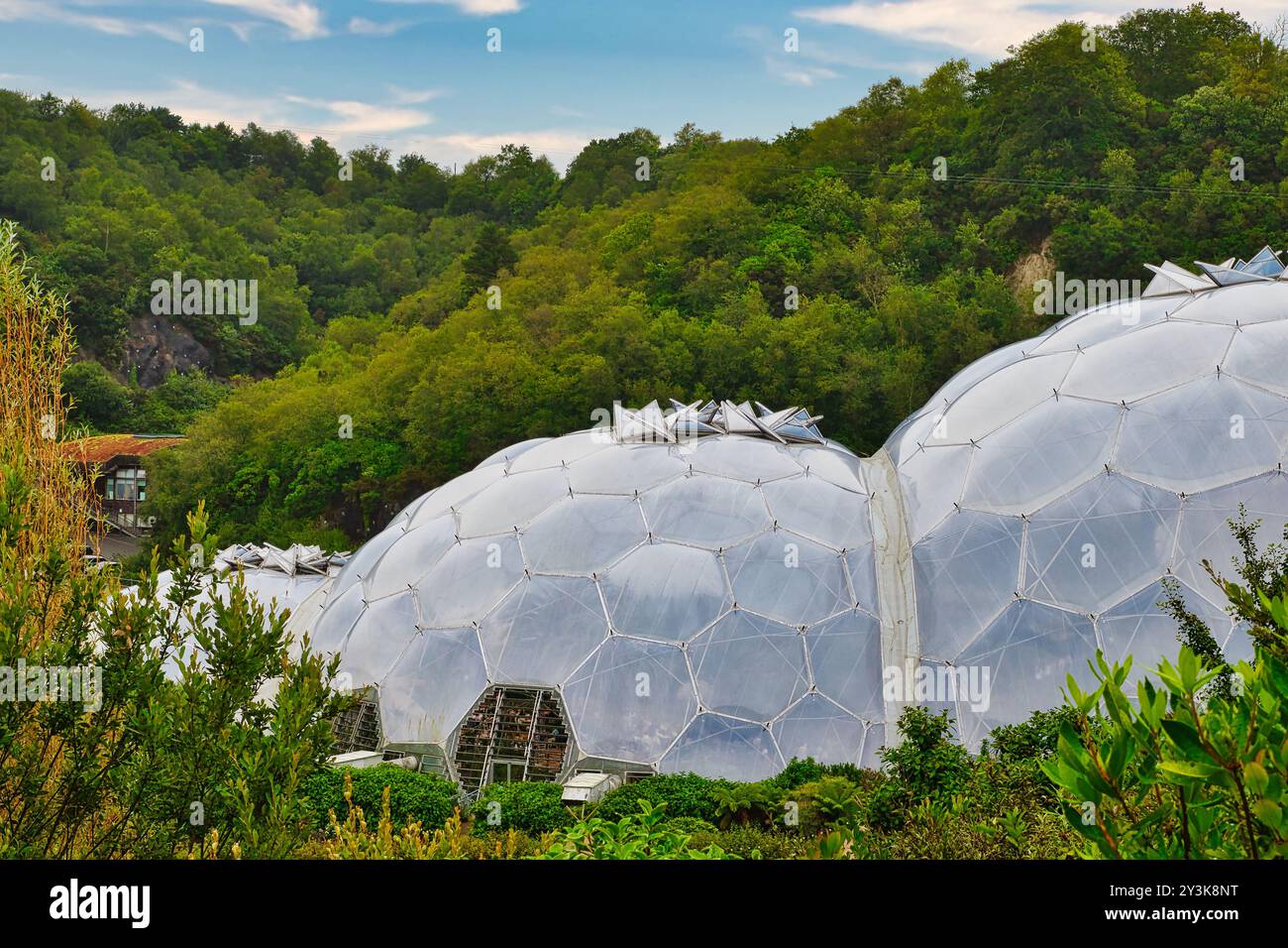 A view of large geodesic domes surrounded by lush greenery, set against a backdrop of hills under a cloudy sky. The domes are made of transparent mate Stock Photo