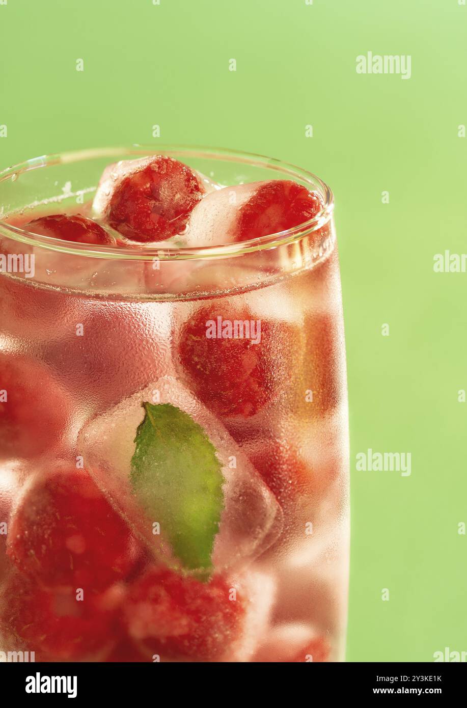Frozen raspberries and mint leaf in a glass of water on a green background. Glass of water with backlight Stock Photo