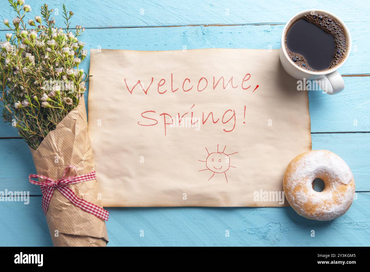 Vintage paper with welcome spring message, handwritten, a bouquet of white flowers and breakfast with coffee and donut, on a blue table. Above view Stock Photo