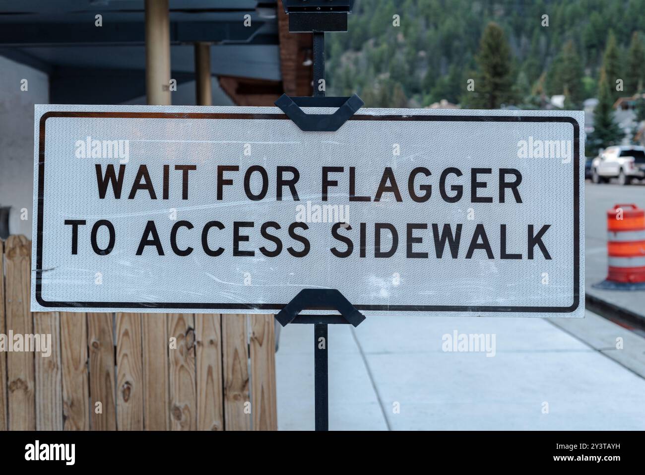 Sign at construction on sidewalk that reads: Wait for flagger to access ...