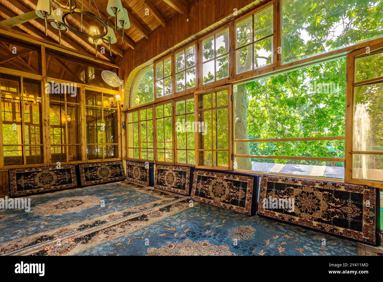 Spacious Traditional Persian Room with Intricate Carpets and Wooden Windows Overlooking Lush Greenery Stock Photo