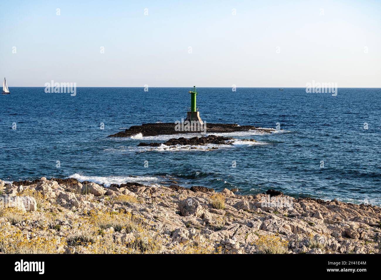 Stacked stone boulders on the top of each other at the Punta Planka cape, Croatia, with green lighthouse signalizing dangerous sea with submerged rock Stock Photo