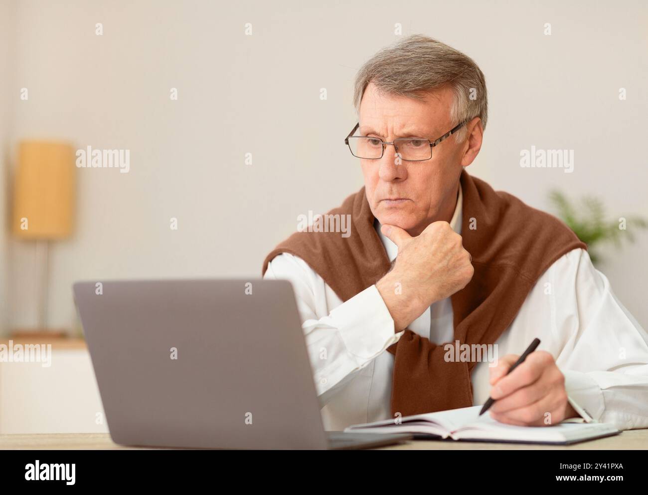 Elderly Man Working On Laptop Taking Notes Sitting In Office Stock Photo