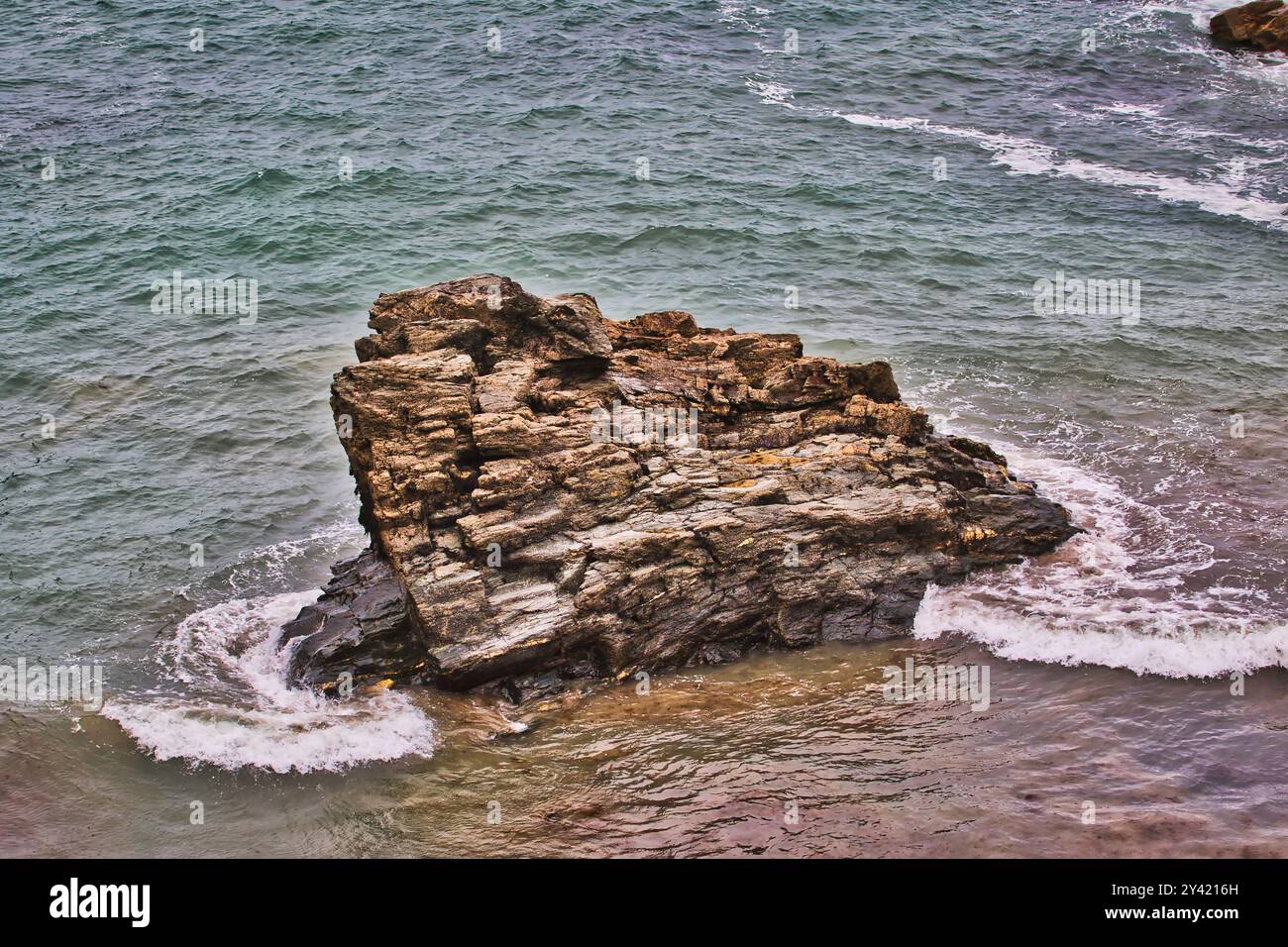 A large, rugged rock formation emerging from the ocean waves ...