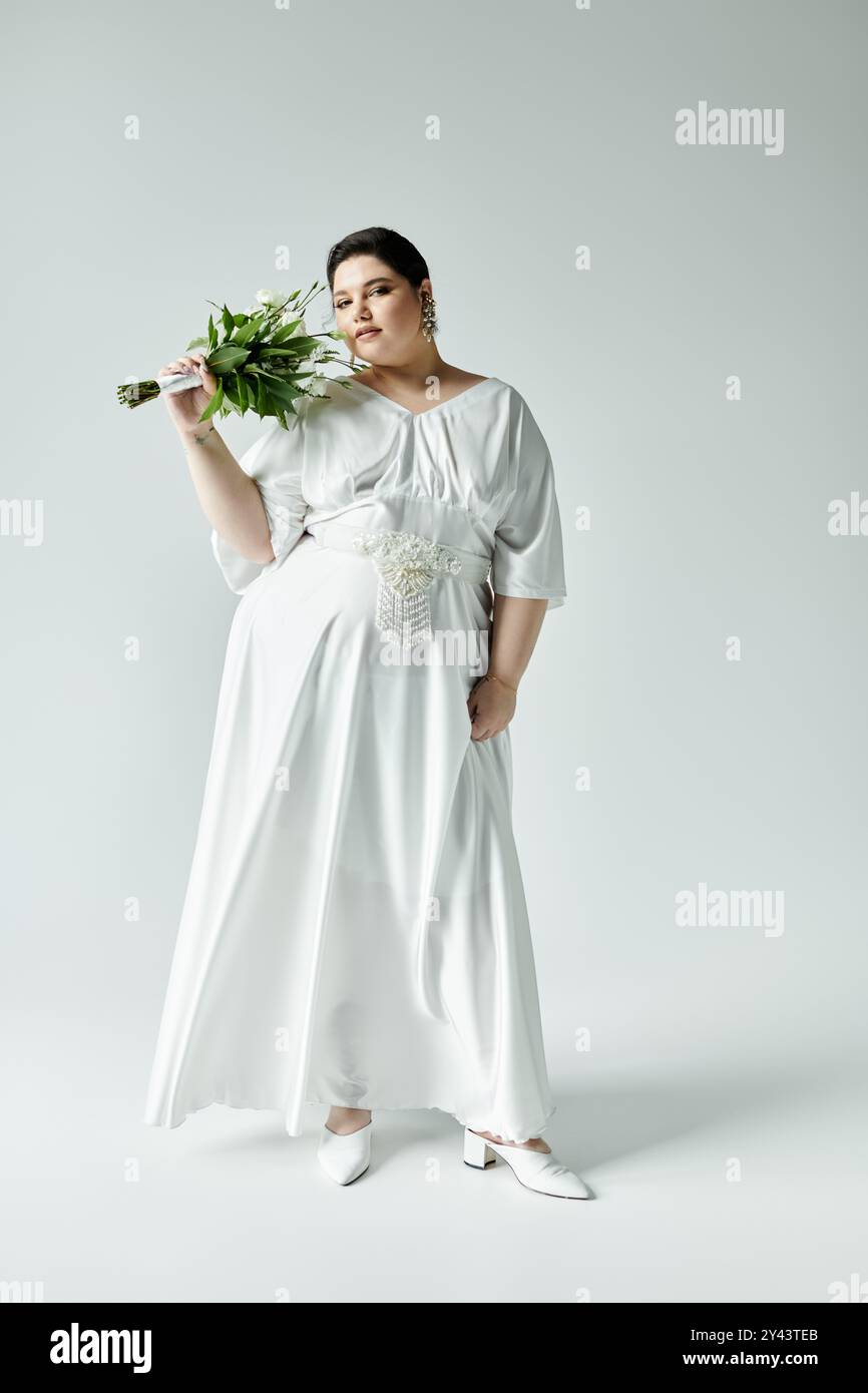 A stunning plus size bride elegantly poses in a white wedding dress with a bouquet, radiating bridal charm. Stock Photo