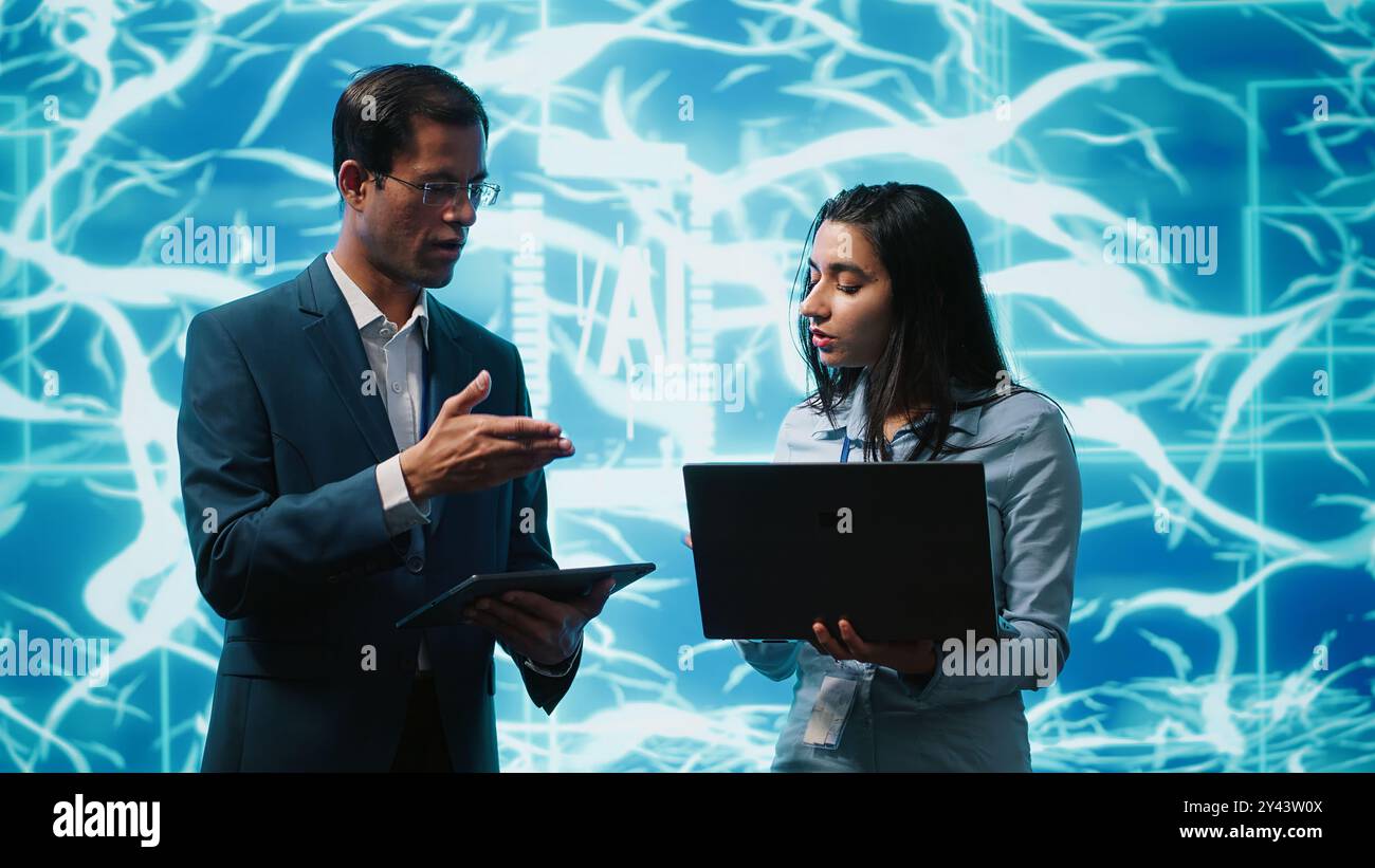 Coworkers solving tasks on laptop and tablet, running artificial intelligence programming scripts. IT staff members using devices to write lines of code for AI applications development, camera A Stock Photo