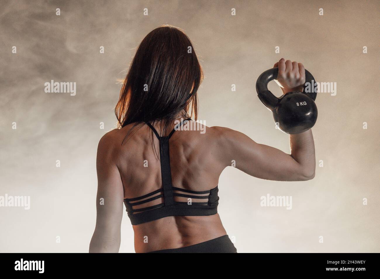 A strong and determined female athlete is engaging in a dynamic workout and lifting a kettlebell in an energized setting that highlights the intensity Stock Photo
