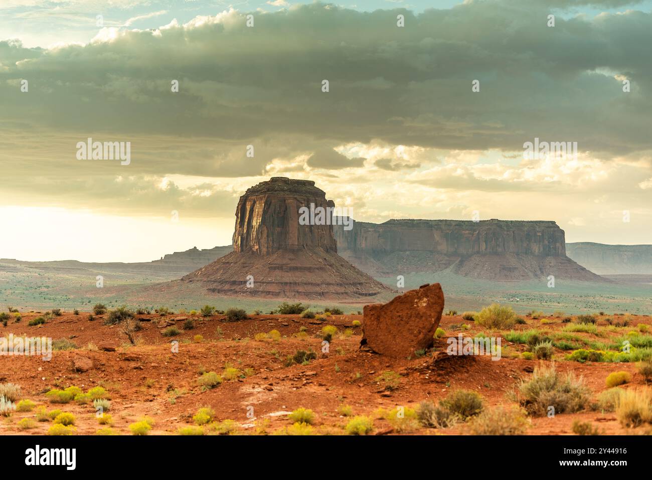 Iconic butte at Monument Valley under a cloudy sky with desert shrubs ...