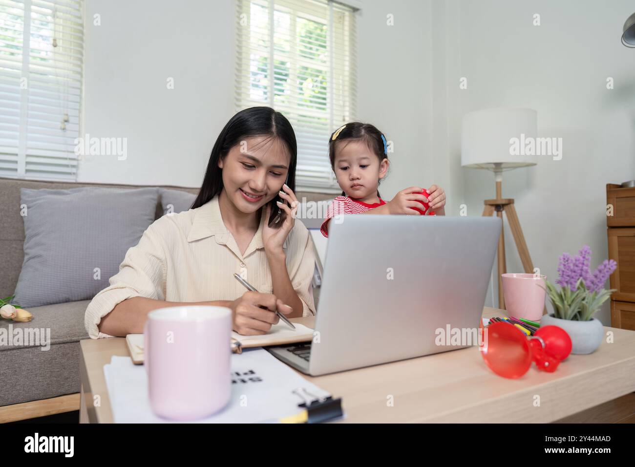 Multi tasking Mother Balances Remote Work and Childcare Using Tech Tools Stock Photo