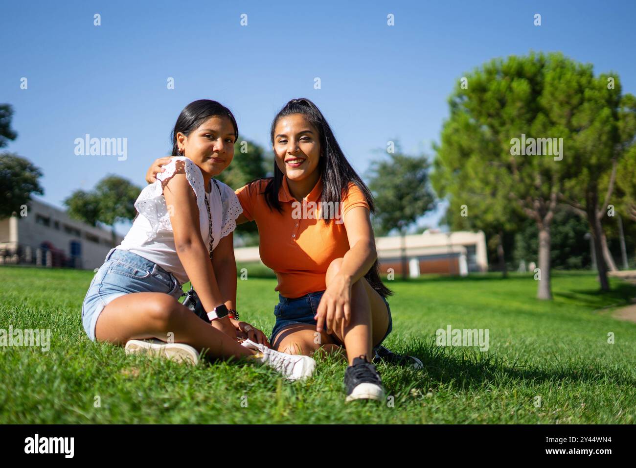 Two Latina sisters together in a park, one a teenager and one a young