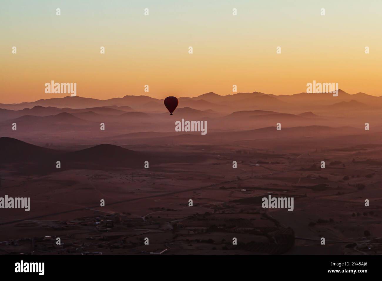 Against a stunning backdrop of undulating dunes, a solitary hot air balloon ascends into the azure sky, embodying the spirit of adventure and freedom. Stock Photo