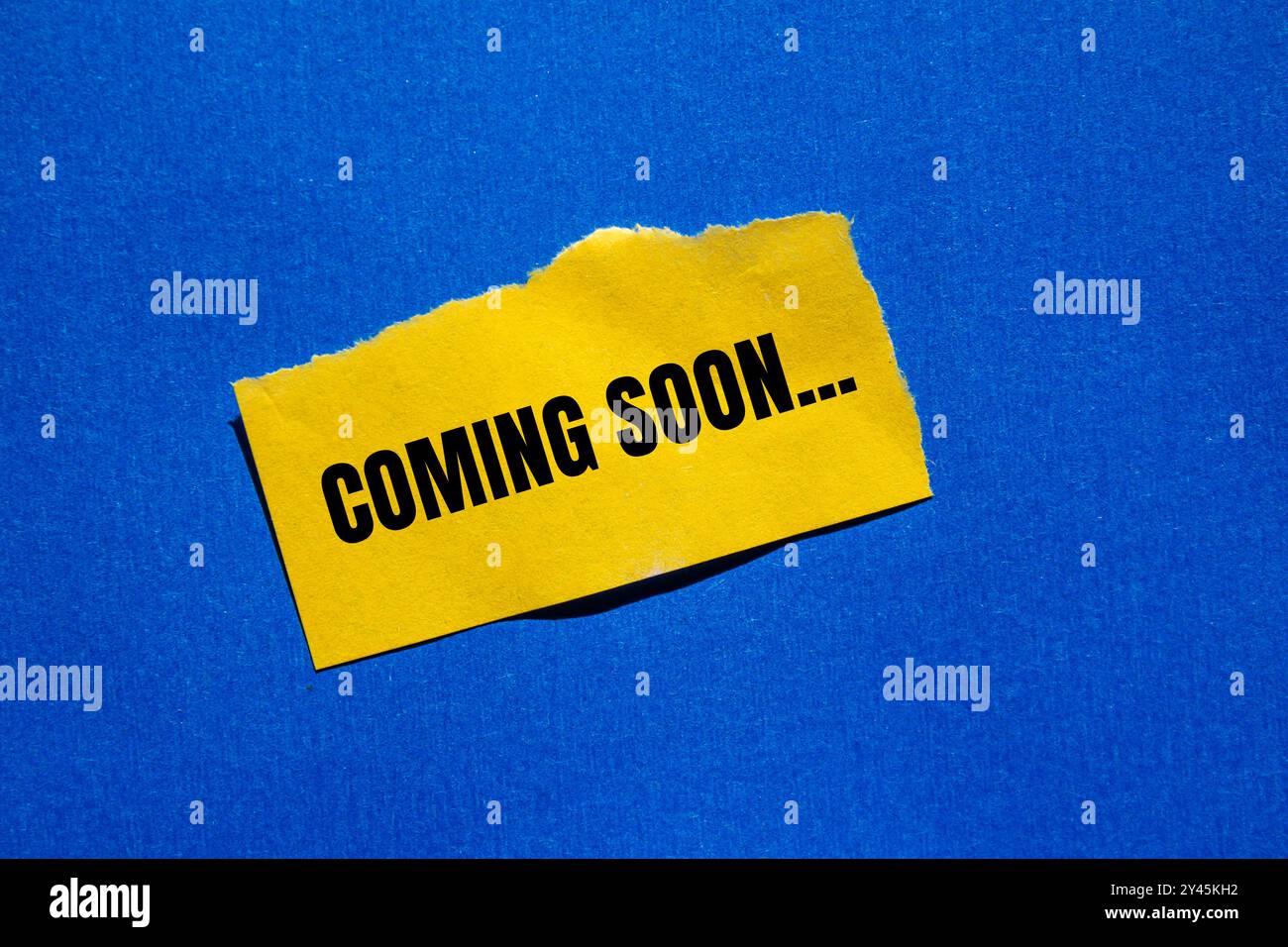 Coming soon message written on ripped torn yellow paper piece with ...