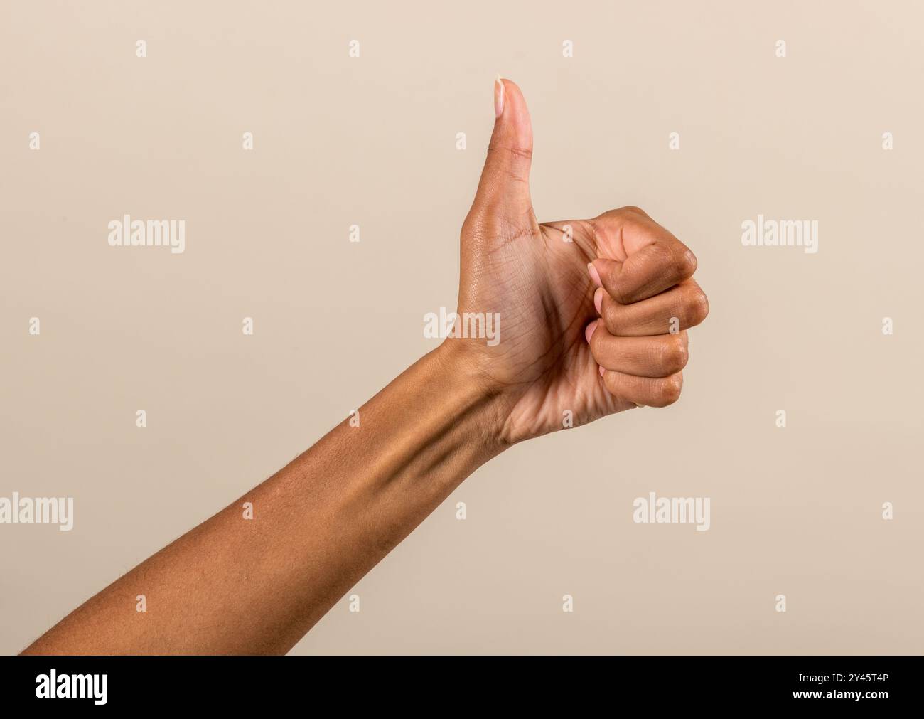 Crop hand of African American female showing thumb up gesture against brown studio background Stock Photo