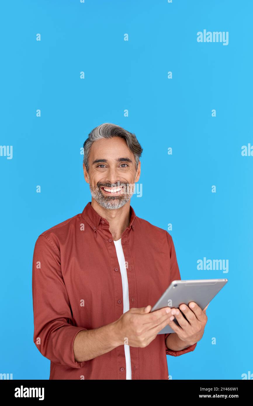 Happy mature man using digital tablet standing isolated on blue background. Stock Photo