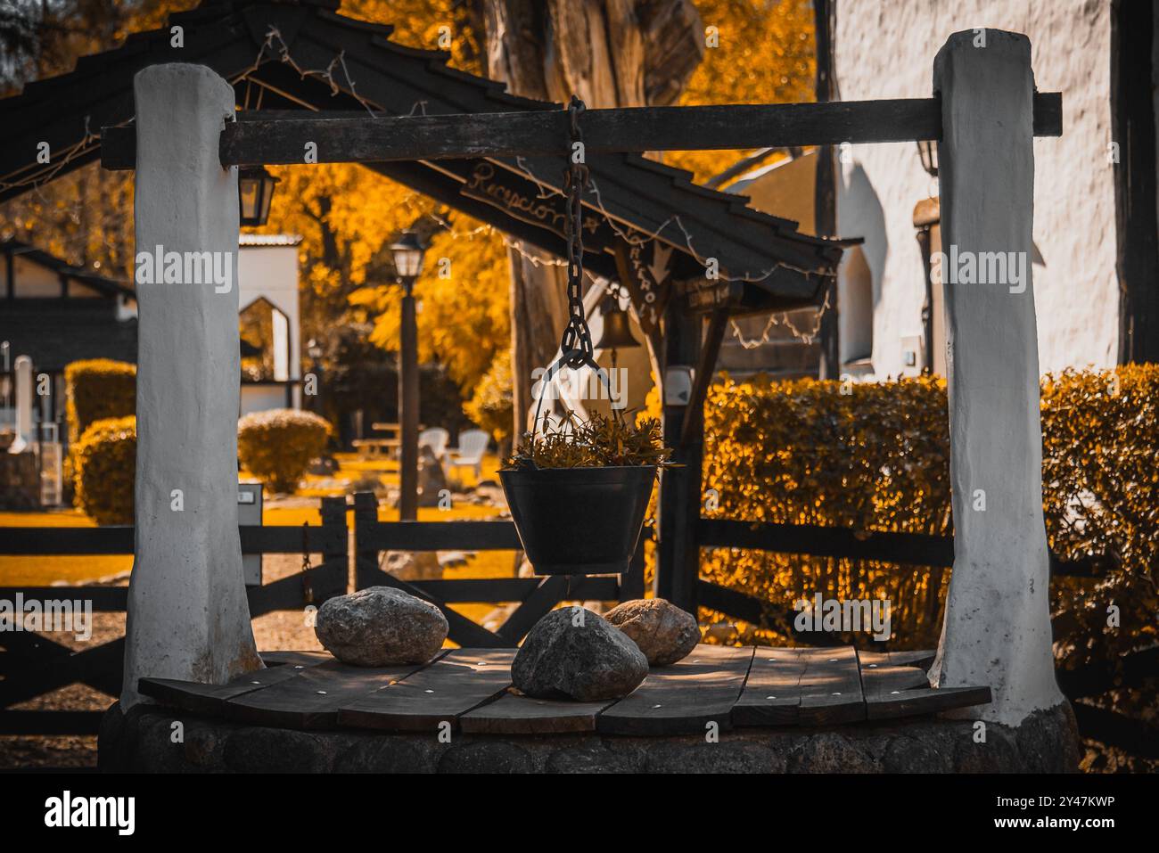 CORDOBA, ARGENTINA, MAY 5, 2022: Old water well made with stone bricks with a decorative bucket filled with flowers hanging from a rusty steel chain Stock Photo