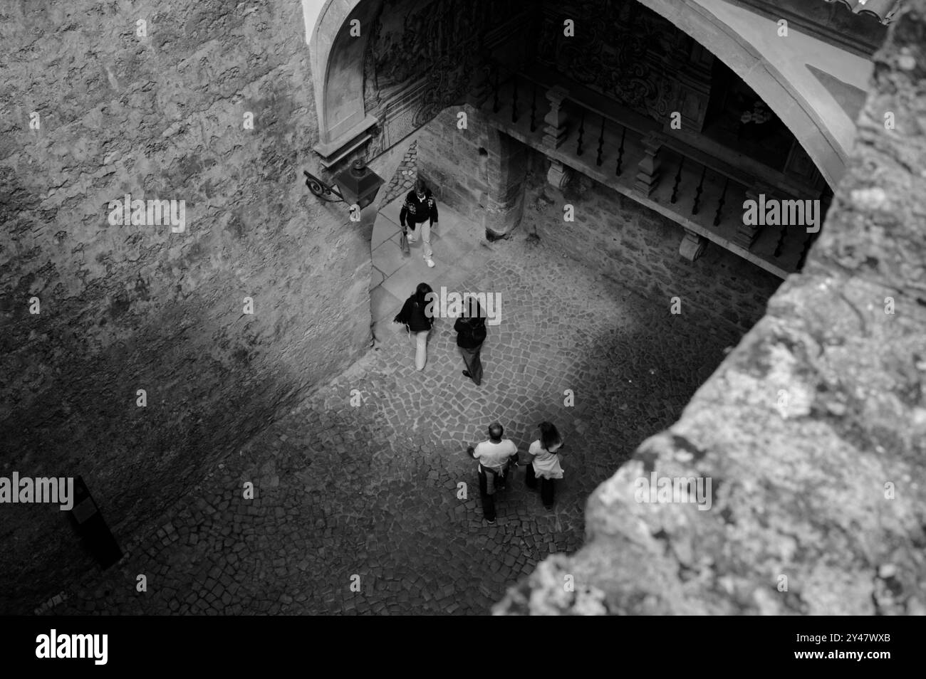 Black and white view of people walking through a cobblestone archway in the medieval streets of Óbidos Stock Photo