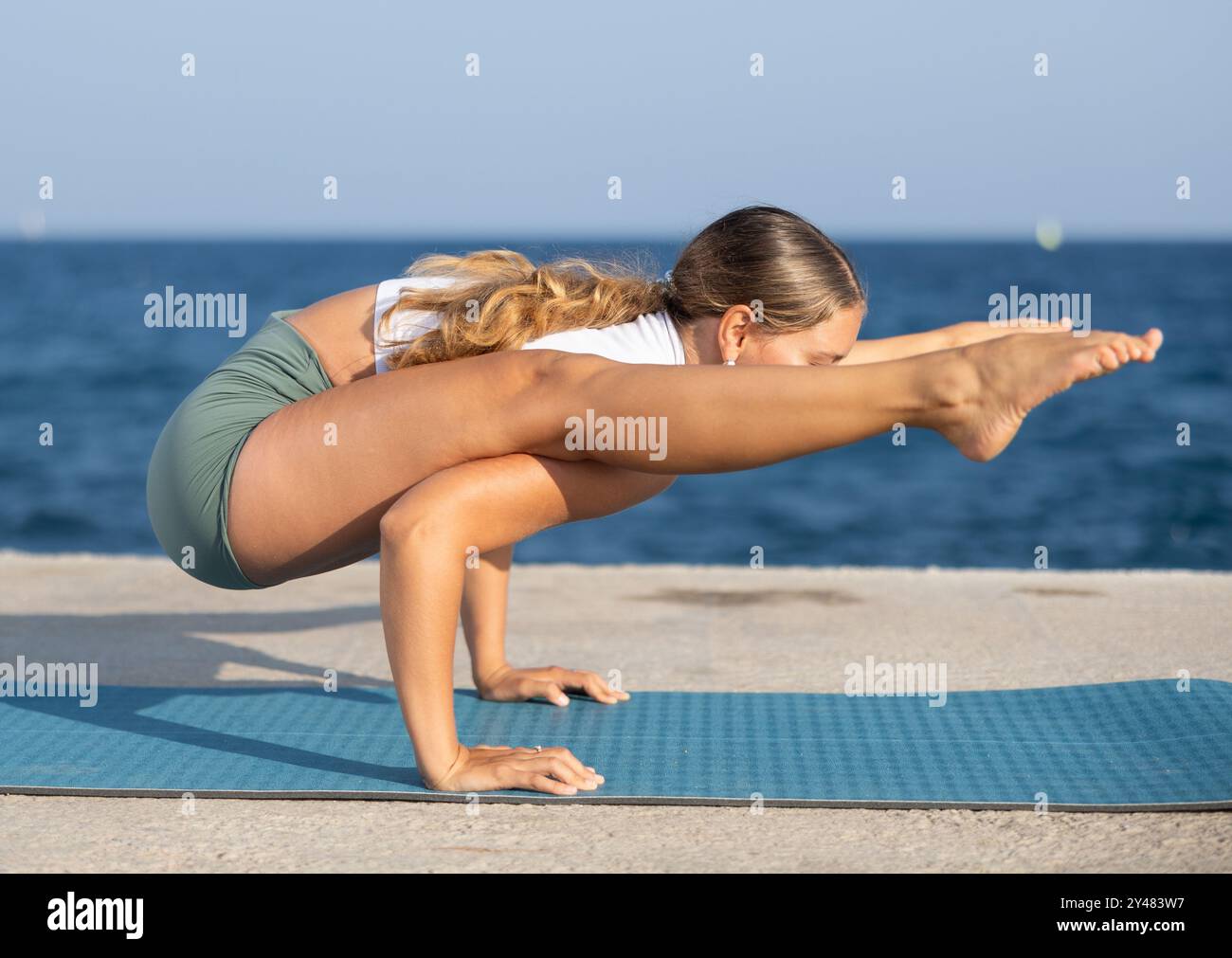 Sportive girl practicing complex pose of yoga on seashore Stock Photo ...