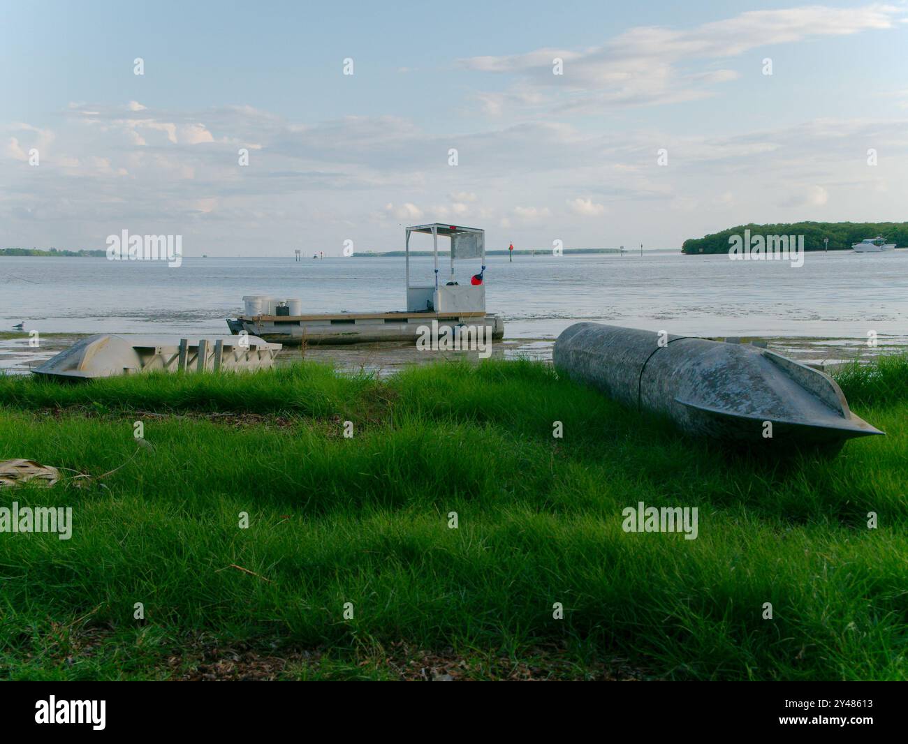 Wide angle view out over metal pontoon tube washed up on shore in green grass to Crab Fishing boat with red ball float Buoys. Over Beach and low tide Stock Photo