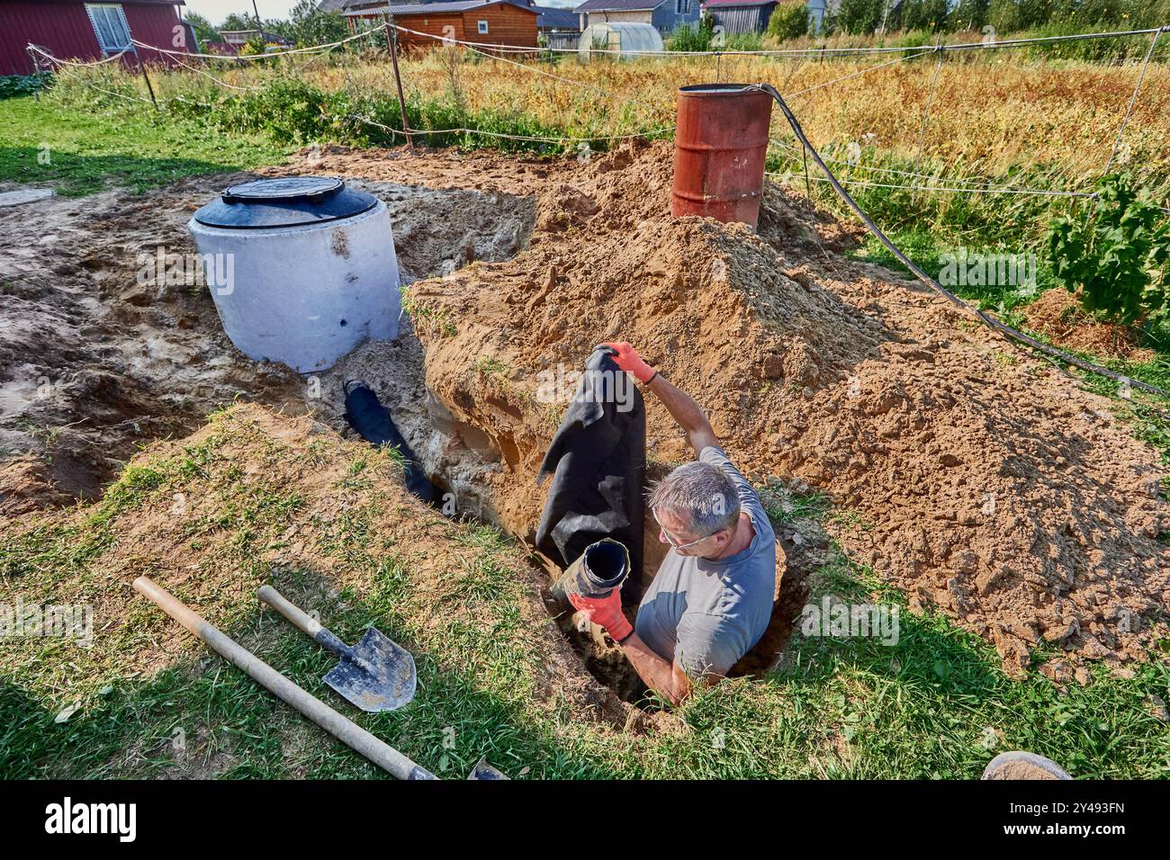 Installation of wastewater plumbing for absorption trenches, worker lays geotextile and perforated sewer drain pipe in trench. Stock Photo