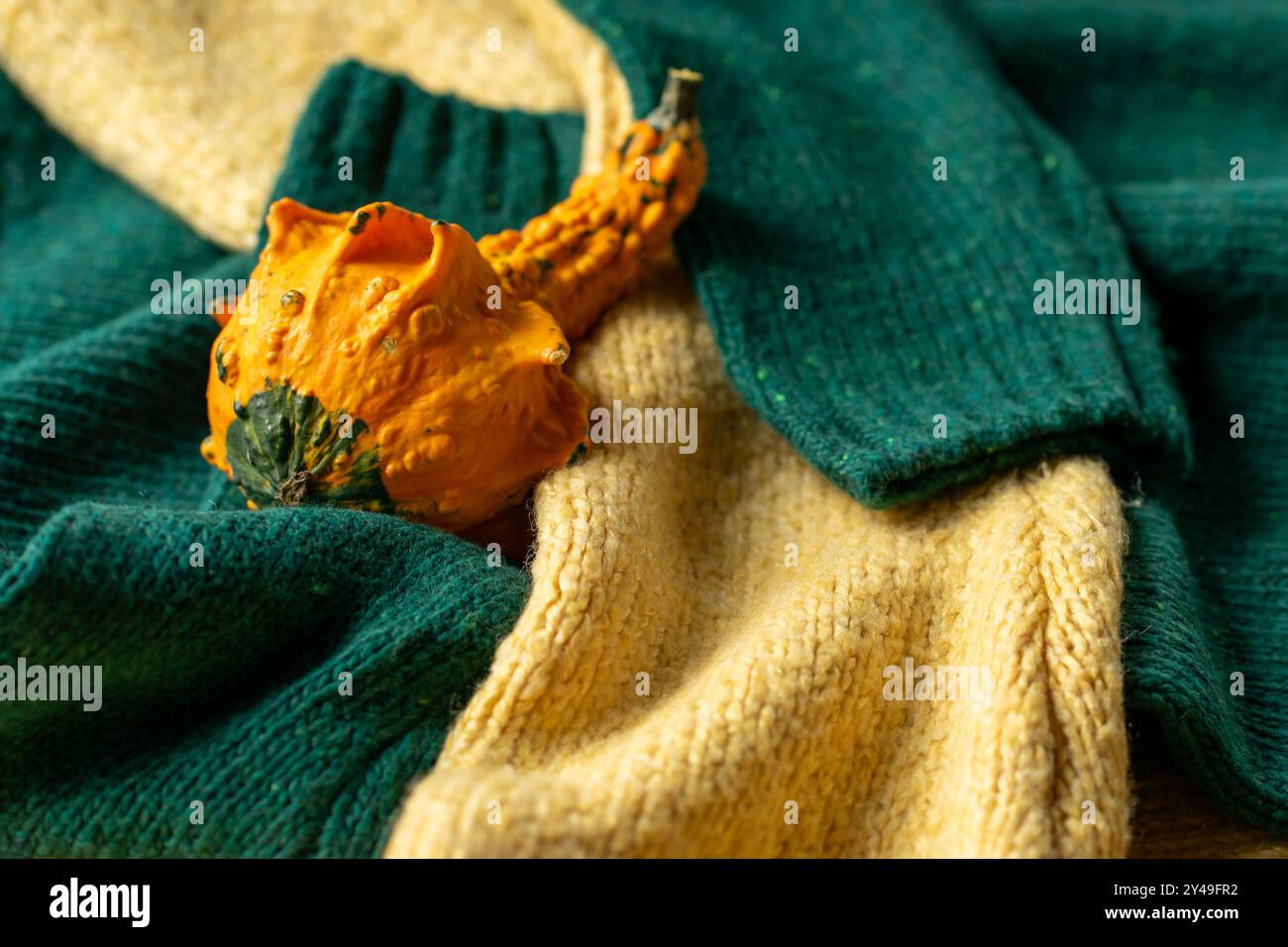 Orange pumpkin near a stack of knitted sweaters on a knitted blanket. Stock Photo