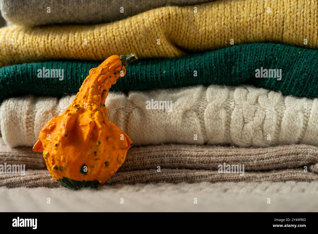 Orange pumpkin near a stack of knitted sweaters on a knitted blanket. Stock Photo