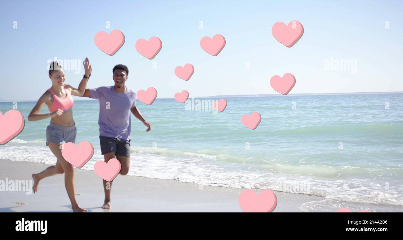 Image of pink hearts over diverse couple running on beach Stock Photo