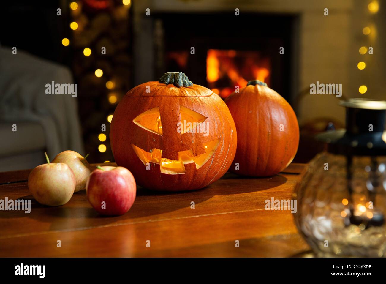 Halloween pumpkin jack-o'-lantern on old wooden table with burning fire place background in a living room on the eve of Halloween, holiday vibes Stock Photo