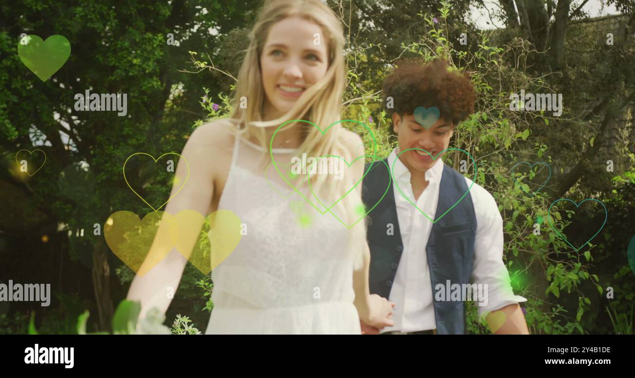 Image of colourful hearts over happy walking in garden on wedding day Stock Photo